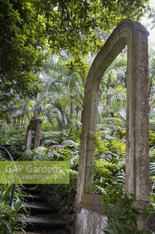 Une série de grands cadres de fenêtres cintrés en pierre situés dans une plantation tropicale et à côté d'un ensemble de marches. Jardins du Monte Palace, Madère. Août. Été 