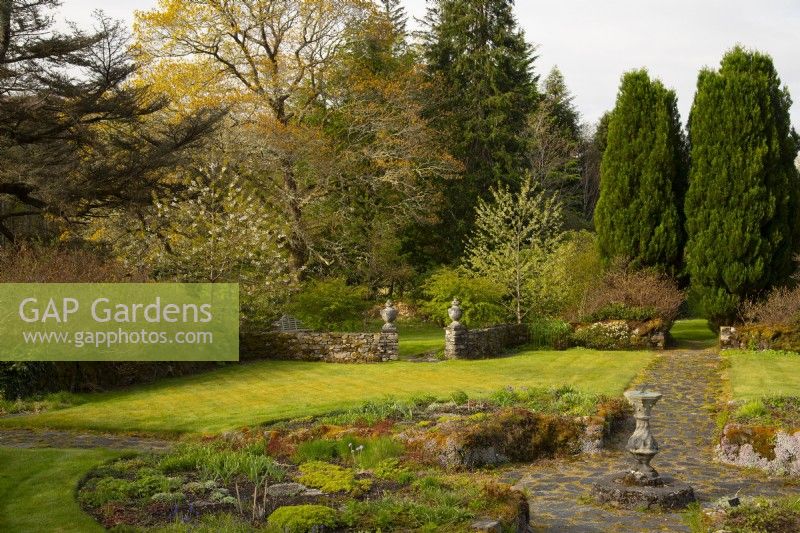 Une vue sur le jardin en contrebas et le cadran solaire jusqu'aux murs de pierre et aux arbres entourant le jardin commémoratif. 