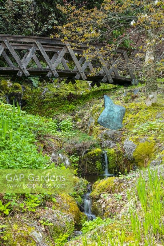 Un pont en bois voûté au-dessus d'une cascade et une sculpture en bronze 'Rapture''. 