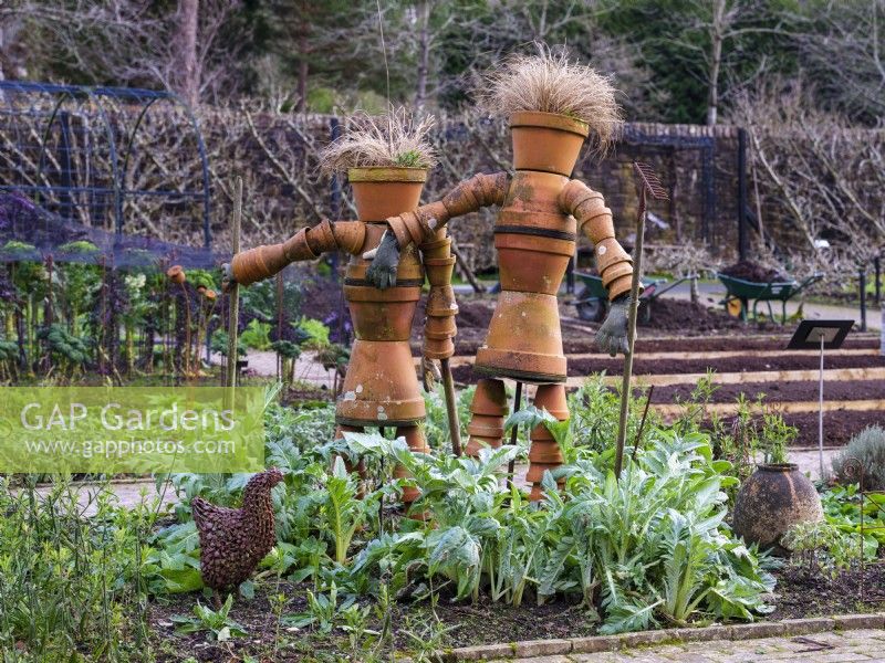 Une paire de jardiniers fabriqués à partir de pots en terre cuite se trouvent parmi des parterres de fleurs surélevés du RHS Rosemoor Garden en février. 