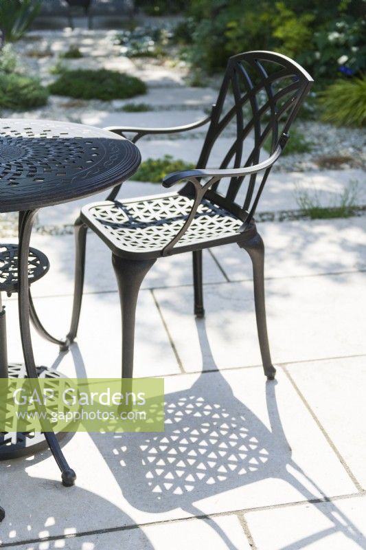 Table et chaise de jardin en alliage d'aluminium projetant des ombres sur le pavage calcaire en été. Juin. 