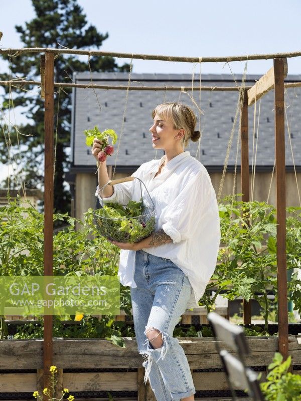 Jeune femme tenant un fil de radis dans un potager urbain, été août 