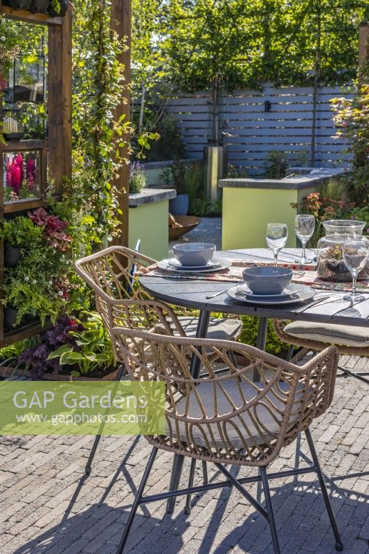 Le coin repas avec table et chaises est entouré d'une pergola en bois avec Trachelospermum jasminoides - Jasmin étoilé, heuchères et fougères. Coin avec foyer à l'arrière. Créateur : Colm Carty 