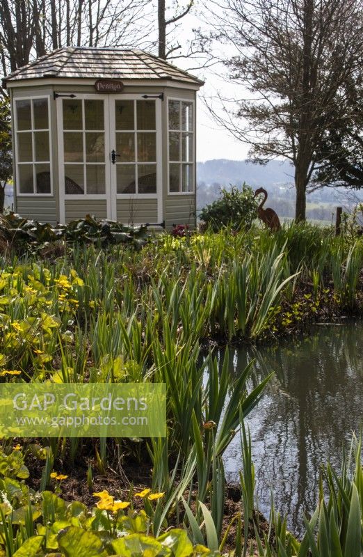 Un pavillon d'été hexagonal en bois à côté d'un étang faunique planté de marginaux à Trench Hill, Gloucestershire 
