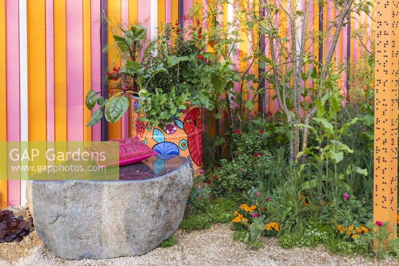 Un banc en pierre, un vieux baril de pétrole peint planté de légumes, d'herbes et de fleurs et un parterre de fleurs vivaces. Le RHS et Eastern Eye Garden of Unity, concepteur : Manoj Malde 