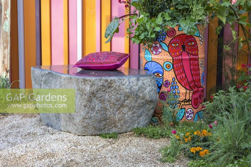 Un banc en pierre avec un coussin rose à côté d'un vieux tambour à huile peint planté de légumes, d'herbes et de fleurs. Le RHS et Eastern Eye Garden of Unity, concepteur : Manoj Malde. 