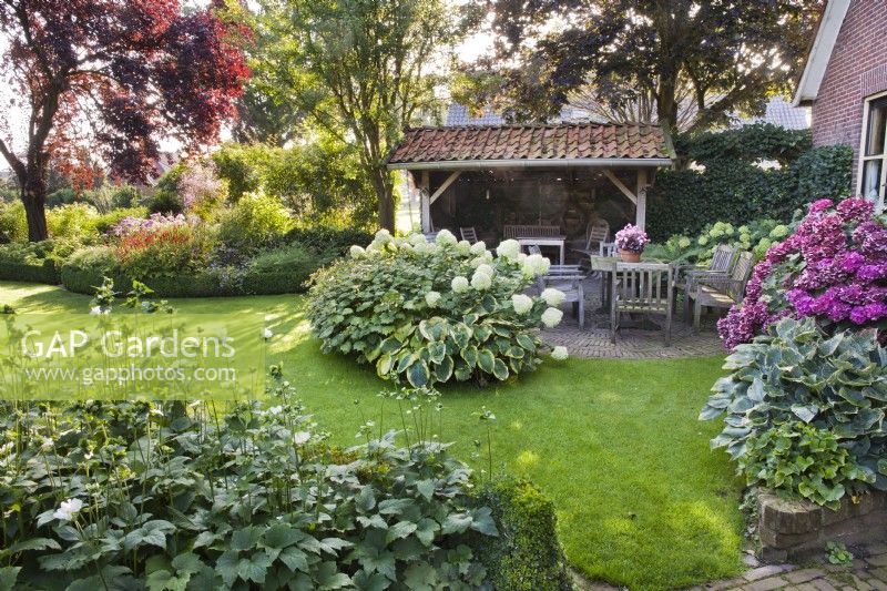 Cour avec salon de jardin et massifs plantés d'Hydrangea arborescens 'Annabelle', Hosta 'Frances Williams', Anémone et Hydrangea macrophylla. 