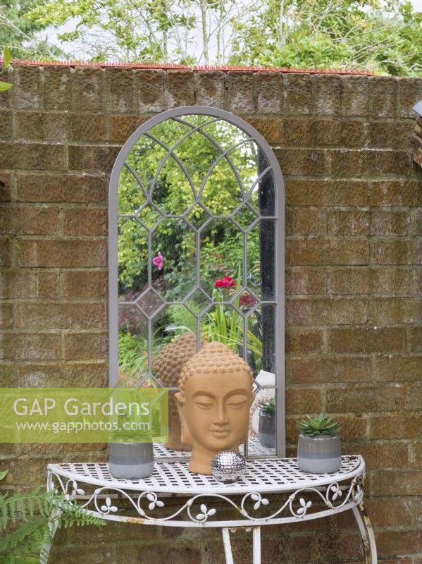Table et miroir en fer forgé contre un mur de briques dans le jardin du cottage 