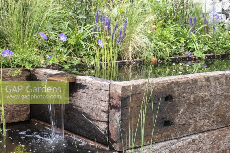 Eau tombant d'un ruisseau dans des étangs fabriqués à partir de traverses récupérées. Toile de fond de plantes, notamment de graminées et de géranium « Rozanne » - Caroline et Peter Clayton - Jardins de démarrage - Nourrir la nature dans la ville, RHS Hampton Court Palace Garden Festival. 