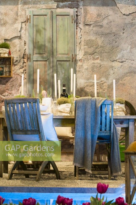 Table décorative préparée pour une soirée de printemps avec des bougies, des verres et des herbes en pot dans la cour italienne contemporaine devant la maison en pierre. Sur la surface du gravier. 