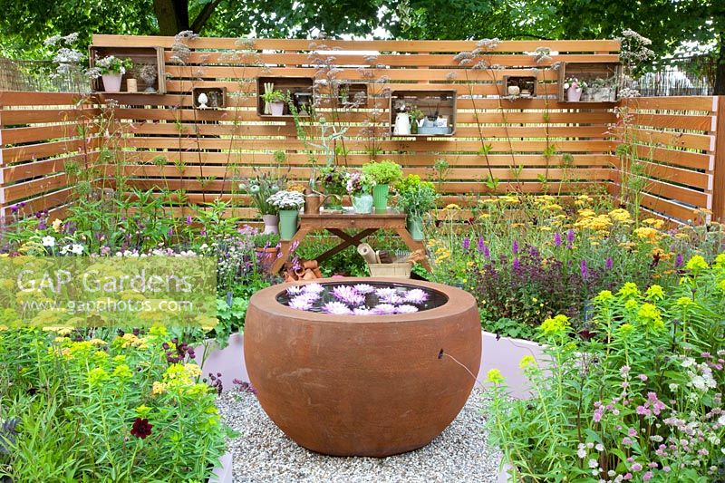Petit jardin avec bol d'eau, table à plantes et étagères sur un mur en bois 