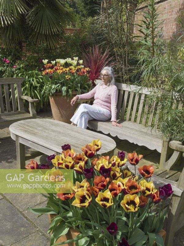 Femme assise dans un coin salon de jardin avec des pots plantés de tulipes 