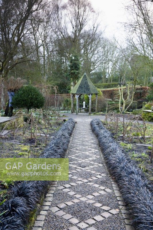 Chemin de gravier avec motif en losange de pavés bordé d'Ophiopogon planiscapus 'Nigrescens' au York Gate Garden en février 