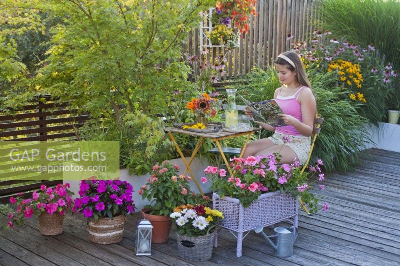 Terrasse d'été colorée avec des fleurs annuelles en pots, une fille aime lire un magazine. 