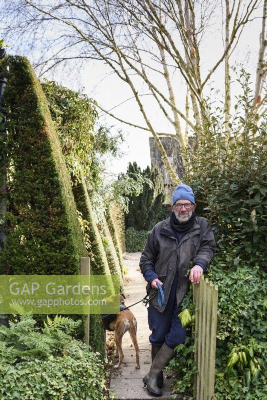 Un homme plus âgé avec son chien appuyé sur la porte de son jardin en janvier 