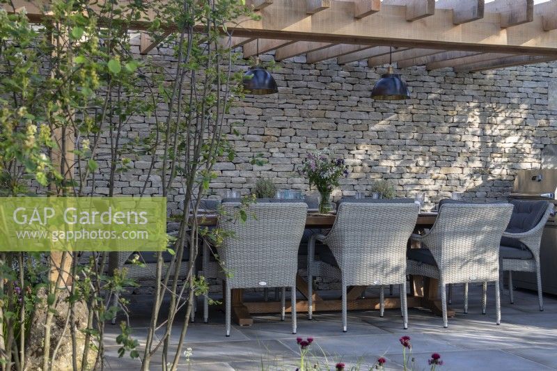 Coin repas extérieur sur une terrasse Yorkstone avec mur en pierre des Cotswolds et pergola en bois sur le jardin des Cotswolds - designer Mark Draper Graduate Gardeners - RHS Malvern Spring Festival 2024 