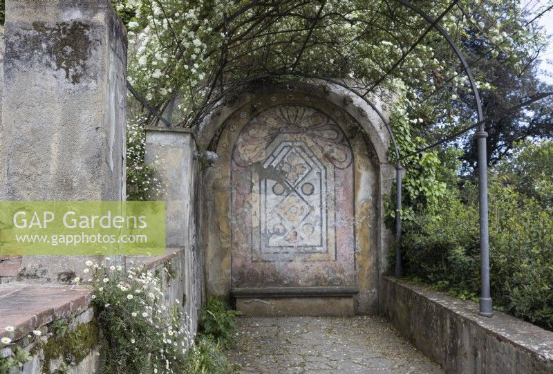 Une vue jusqu'au bout de la Rose Arbor avec un mur d'extrémité peint d'origine. Une rose blanche fleurit au-dessus de la tonnelle. Jardins Bardini, Florence. 