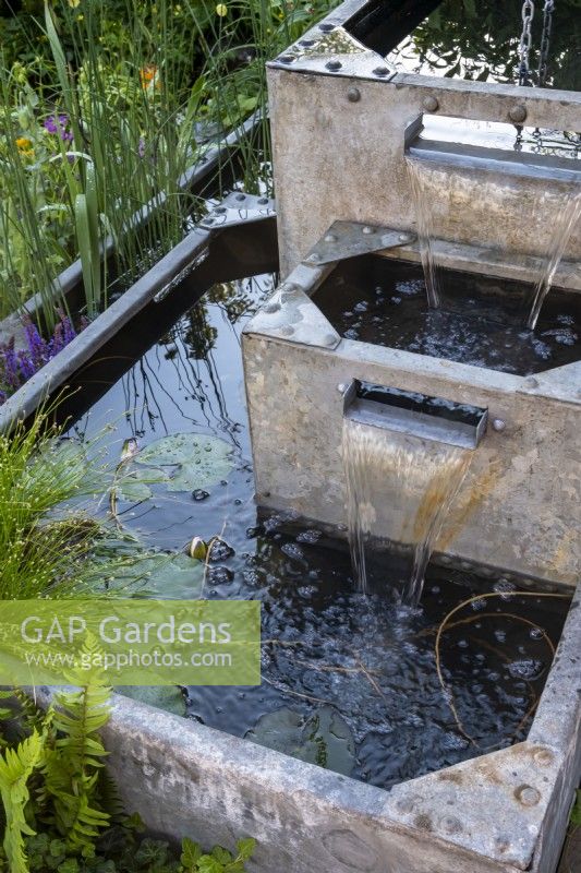 Une série d'abreuvoirs galvanisés avec de l'eau qui coule les reliant tous ensemble sur le jardin résilient aux inondations : conçu par Naomi Slade et Ed Barsley, sponsor : Flood Re 