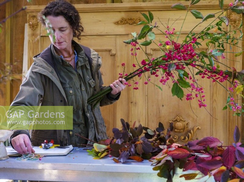 Atelier intérieur de grange où Zanna Hoskins, fleuriste spécialisée dans le feuillage, travaille avec des fruits et des feuilles d'automne récoltés dans son jardin pour les utiliser dans des compositions saisonnières. Novembre, automne, Dorset, Royaume-Uni. 