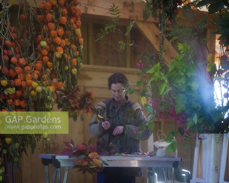 Atelier intérieur de grange où l'on voit ici reflété dans un miroir, fleuriste spécialisée dans le feuillage, Zanna Hoskins travaille avec des fruits d'automne et des feuilles récoltées dans son jardin pour les utiliser dans des compositions saisonnières. Novembre, automne, Dorset, Royaume-Uni. 