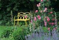 Jardin d'été avec banc en métal jaune et obélisque rose