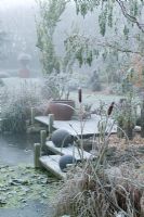 Un matin brumeux et givré près de l'étang gelé du jardin de John Massey. Statue, urne et pot agissant tous comme points focaux. Terrasse en bois avec des boules de bronze. Des taureaux au premier plan.