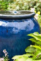 Fontaine à bulles dans un pot en céramique émaillée bleu avec des feuilles d'Hosta.