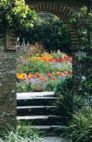 Regardant à travers l'arche dans le jardin de la grange à Great Dixter au printemps. Tulipa 'Prinses Irene' au premier plan.