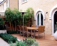 Terrasse en bois à côté de la maison avec table et chaises, Phyllostachys vivax 'Aureocallis' et Buxus