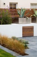 Jardin minimaliste par Wynniatt-Husey Clarke. Stipa tenuissima dans un patio en ardoise grise avec des pots en métal plantés d'Agaves derrière