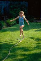 Jeune fille jouant avec un tuyau d'arrosage dans le jardin