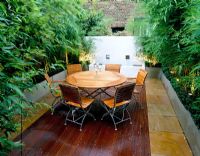 Terrasse sur le toit avec terrasse en bois la nuit - Table et chaises en bois, pots en métal galvanisé avec bambou et mur blanchi à la chaux