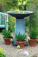 Pièce d'eau contemporaine en pierre bleue avec bol dans le jardin sur gravier avec des pots d'Agapanthus. Banc de jardin bleu avec porte au-delà