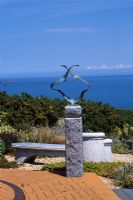 Jardin en bord de mer à Guernesey avec vue sur la mer avec terrasse en brique, gravier, assise en granit chinois et sculpture 'Mouettes' de Guy Portelli