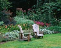 Deux chaises adirondacks devant un parterre de fleurs avec Liatris, Hemerocallis et Eupatorium