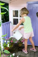 Jeune fille arrosant des pots d'Impatiens - Lizzies occupés avec arrosoir à l'extérieur de la maison wendy peinte