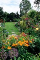 Jardin de campagne rempli de fleurs de style traditionnel avec Rosa 'Marjerie Fair', Rosa 'Sadlers Wells', Alstroemeria, Allium christophii, Allium giganteum et Phormium