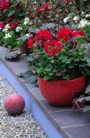 Pot en béton rouge planté de Pelargoniums, avec sphère en béton rouge
