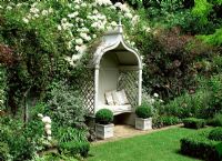 Gazebo classique avec banc et coussins dans un jardin à la française. Rosa 'Kiftsgate', Teucrinum, Cotinus, Buxus sempervirens - Boîte de balles topiaires