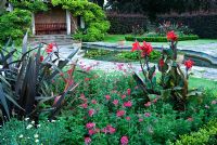 Jardin formel avec étang de nénuphars, parterre de fleurs avec Buxus - Parterres de fleurs bordés de cannes, de verbènes et de Phormium tenax à Kingston Maurward Gardens, Dorchester, Dorset