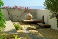 Jardin moderne avec gravier, pierres ornementales, globes et mur peint avec des fleurs rouges grimpantes - Santa Barbara, USA