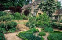 Chemins de gravier, marches et parterres surélevés dans un jardin d'herbes aromatiques devant la maison - Hinton House, Bibury