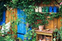 Un pavillon d'été en bois avec des plantes mélangées et des nichoirs peints à l'extérieur