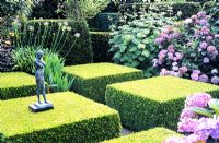 Jardin à la française avec des formes de Buxus coupées et une petite statue figurative