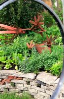 Jardin construit à partir de matériaux recyclés - Fenêtres fabriquées à partir de roues de vélo, sculptures de poulet fabriquées à partir de vieilles pièces de tondeuse et sous-plantées de légumes et d'herbes