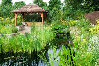 Une maison d'été et un coin salon en contrebas entouré d'un étang avec des plantations aquatiques et marginales dans le monde du jardin d'eau au RHS Hampton Court Flower Show