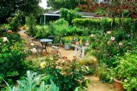 Chemin à travers les parterres de Rosa, légumes et herbes avec table et chaises de style café - Le jardin Krause, Santa Barbara, USA