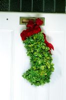 Bas de Noël sur la porte d'entrée remplie de mousse et recouvert de petits brins d'euonymus à feuilles persistantes et d'œillets en aérosol rouge