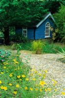 Maison d'été peinte en bleu sous les arbres avec jardin de gravier. Conçu par Alan Titchmarsh à Barleywood, Hampshire.