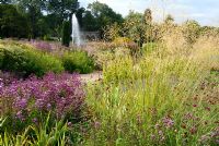 Fontaine avec plantation de plantes vivaces et d'herbes mixtes, dont Origanum, Eryngium, Geranium, Knautia et Stipa gigantea en premier plan - Les jardins italiens de Trentham, en août.